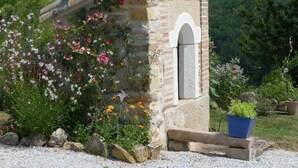 Estructura de piedra con techo de madera, rodeada de diversas plantas en flor y un pequeño jardín.
