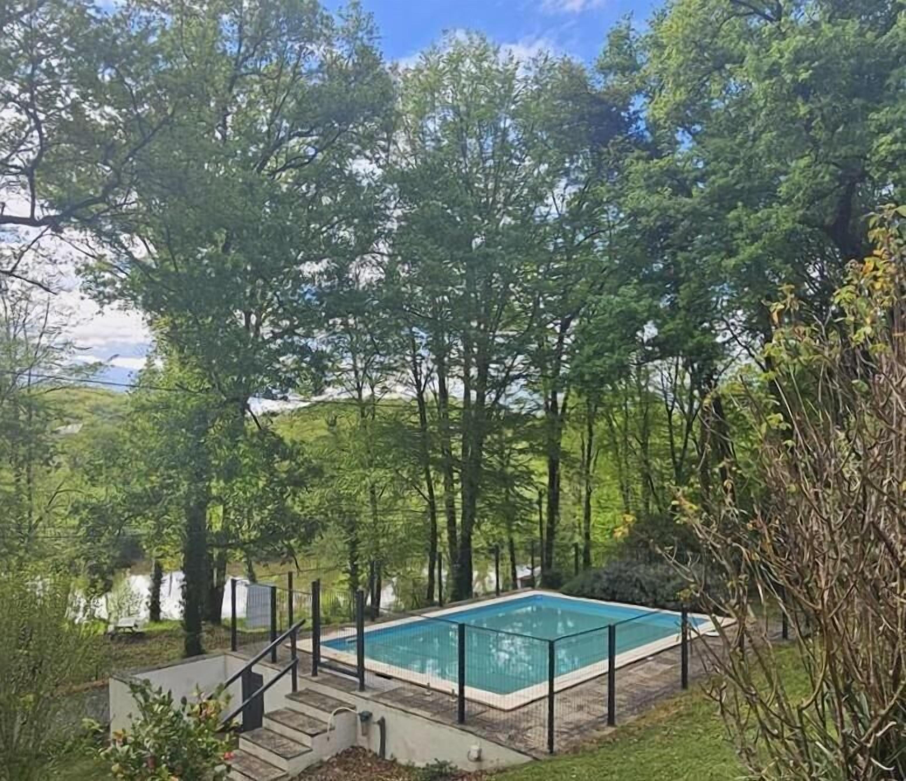 A rectangular swimming pool surrounded by a metal fence, with a staircase leading down to the pool.