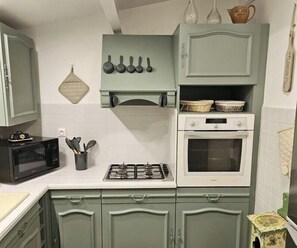 Una cocina con microondas, estufa y horno, con gabinetes verdes y encimeras blancas.