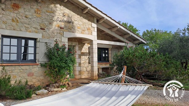 A stone building with a hammock in the foreground, a stone wall, and a wooden deck. - La Montarnaude - PUYCELSI (PUYCELSI)