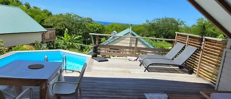 Eine Holzterrasse mit Pool, Liegestühlen und einem Tisch.