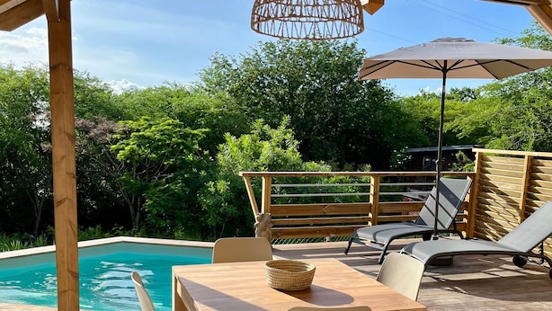 Eine Terrass mit Holztable und -stühlen, einem Pool und einem Pergola mit einer hängenden Leuchte.