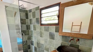 Ein modernes Badezimmer mit einer gläsernen Duschkabine, einem Holzwaschtisch mit Steinbecken und einem kleinen Fenster, das für natürliches Licht sorgt.