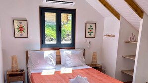 Un dormitorio con una cama de madera, una colcha roja, una ventana con vistas a follaje y un ventilador de techo.