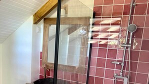 Un baño moderno con ducha envuelta en vidrio, tocador de madera con un lavabo grande y paredes de azulejos rojos.