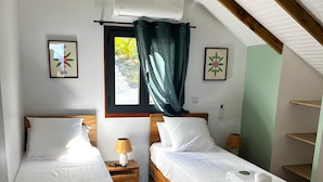 Habitación de hotel con dos camas de madera, una ventana con cortinas, un equipo de aire acondicionado y una mesita de noche con lámpara.