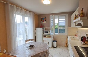 A compact kitchen with a dining area, a refrigerator, a microwave, and a sink. There is a window with curtains, a painting on the wall, and a logo on the counter. - Le Flamenco - Albi - City break (Albi)