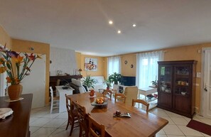 A dining area with a wooden table, chairs, and a vase of flowers. There is a sofa and a television in the background. - Le Flamenco - Albi - City break (Albi)