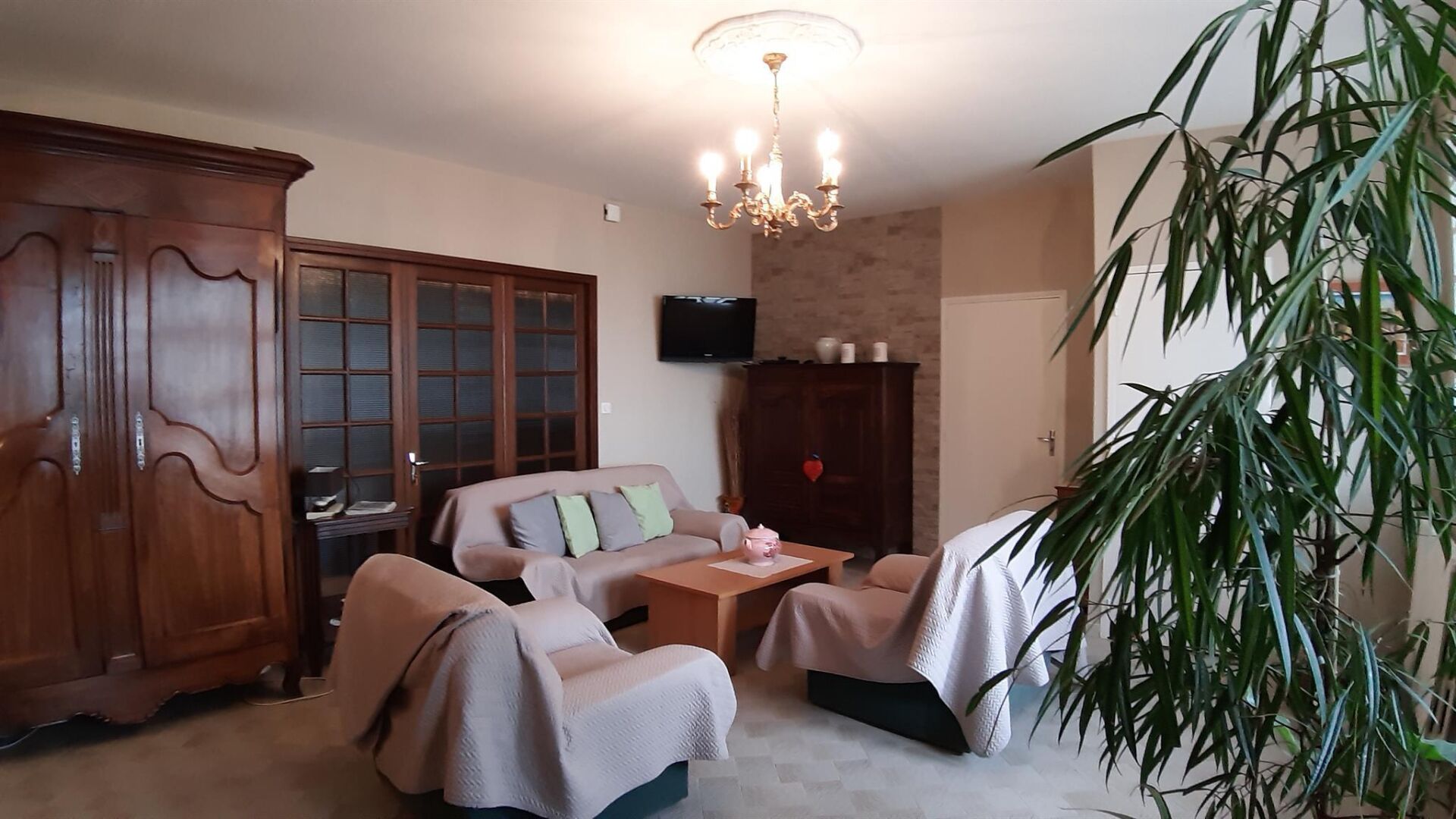 Una sala de estar con un sofá, dos sillones, una mesita de centro, un televisor, un aparador de madera y una planta grande.