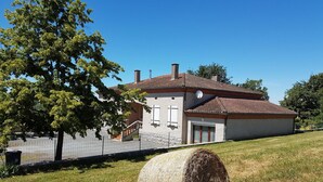 A house with a tiled roof, a satellite dish, and a large tree in the foreground.