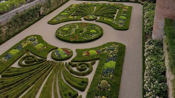 A meticulously landscaped garden with geometric patterns and a view of a historic building in the background.