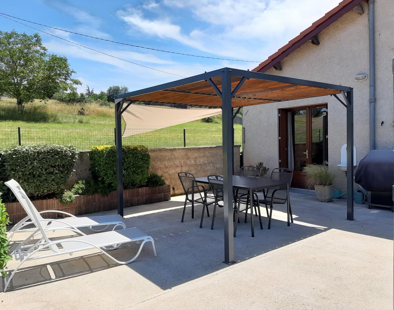 A covered patio area with a table and chairs, a grill, and a white lounge chair.