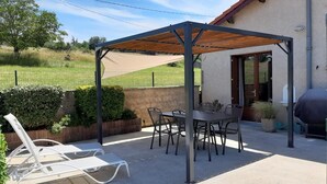A covered patio area with a table and chairs, a grill, and a white lounge chair.