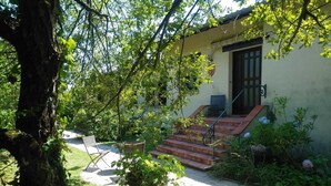 A house with a garden, a patio with a table and chairs, and a staircase leading to the entrance.