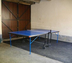Deux tables de ping-pong portables, équipées de roulettes, sont placées sur un sol en béton, adossées à un mur où se trouve une porte en bois.