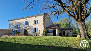 A two-story stone building with blue shutters, a small attached structure, and a well-maintained lawn. - Bonnefon - CESTAYROLS (CESTAYROLS)