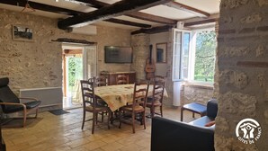 A rustic dining area with a wooden table and chairs, a guitar, and a television on the wall. - Bonnefon - CESTAYROLS (CESTAYROLS)