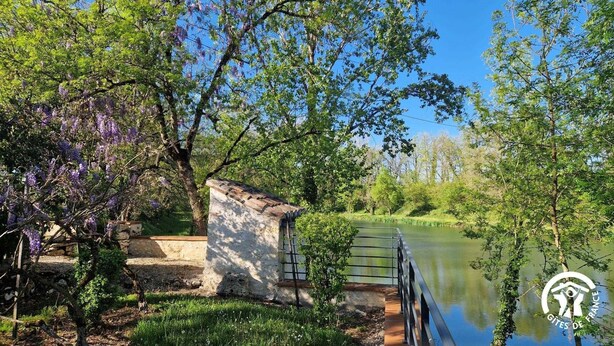 A serene riverside setting with a stone structure, lush greenery, and a clear blue sky. - Bonnefon - CESTAYROLS (CESTAYROLS)