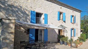 A stone building with blue shutters, a covered outdoor seating area, and potted plants. - Bonnefon - CESTAYROLS (CESTAYROLS)