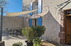 Un edificio rústico de piedra con una puerta de madera, una mesa con sillas y una planta en maceta.
