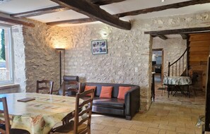 Un interior rústico con paredes de piedra vista, techo de madera, zona de comedor con mesa y sillas, y un rincón acogedor con sofá.