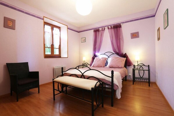 Un dormitorio con cama, una silla, un banco, una ventana y una mesita de noche.