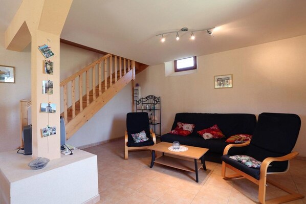 A living room with a wooden staircase, a black sofa, two armchairs, a small table, and a wall with photos. - Combefa - TONNAC - Gîte (TONNAC)
