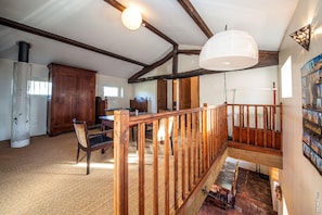 A spacious room with a high ceiling, wooden beams, a dining area with a table and chairs, and a staircase with a wooden railing.