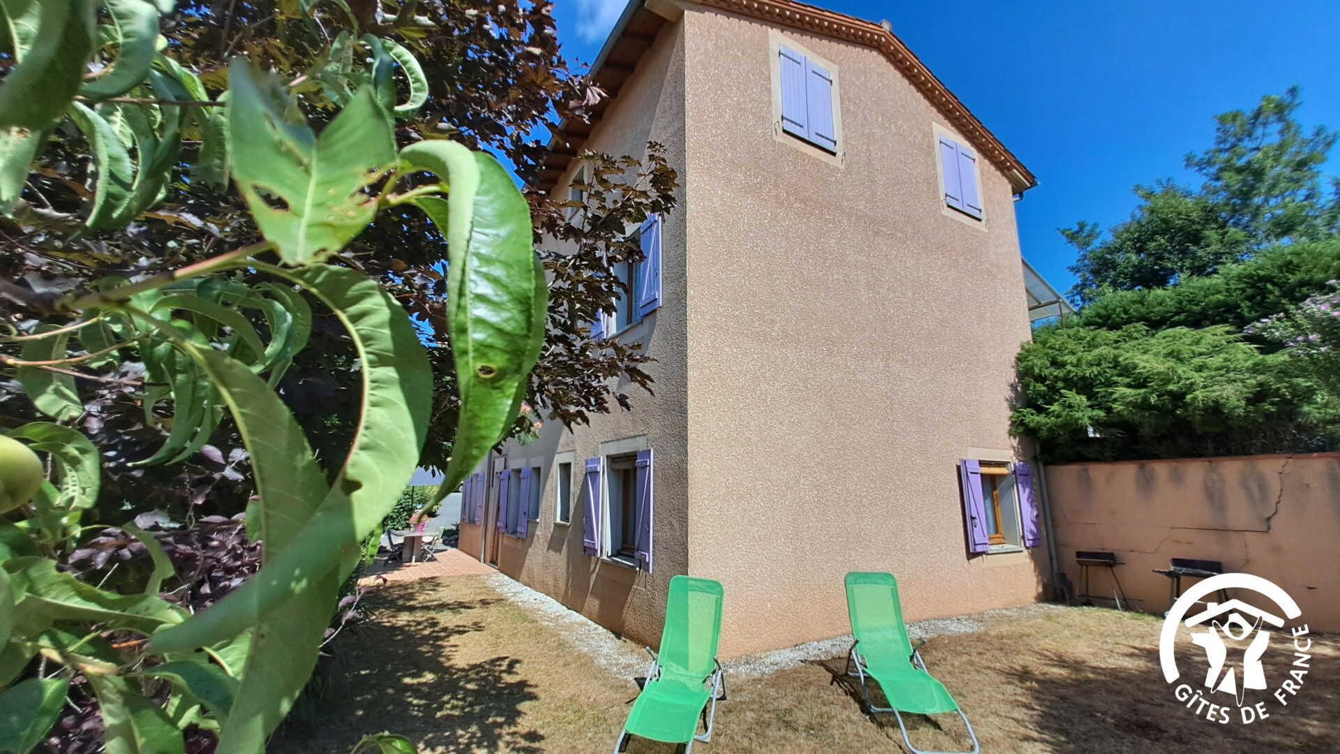 Ein zweistöckiges Gebäude mit sandfarbener Fassade, einem kleinen Balkon und einem grünen Stuhl im Vordergrund.
