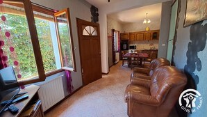 A living room with a brown leather sofa, a dining table with chairs, a kitchen area with wooden cabinets, and a window with a view of greenery. - La Bruninquillé - MONTREDON-LABEISSONNIE (MONTREDON-LABEISSONNIE)