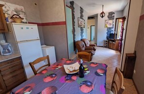 A dining area with a table set for two, a refrigerator, a coffee maker, and a chair. - La Bruninquillé - MONTREDON-LABEISSONNIE (MONTREDON-LABEISSONNIE)