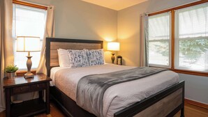 Une chambre à coucher avec un lit, des tables de chevet, des lampes et une fenêtre avec des stores.