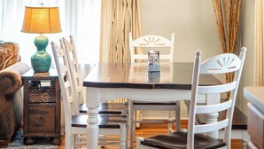 Un coin repas comprenant une table en bois, des chaises blanches, une lampe et une petite table d’appoint avec un panier.
