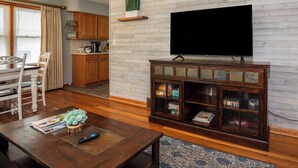 Un salon avec un meuble TV en bois, une table à manger avec des chaises et un coin cuisine doté de meubles en bois.