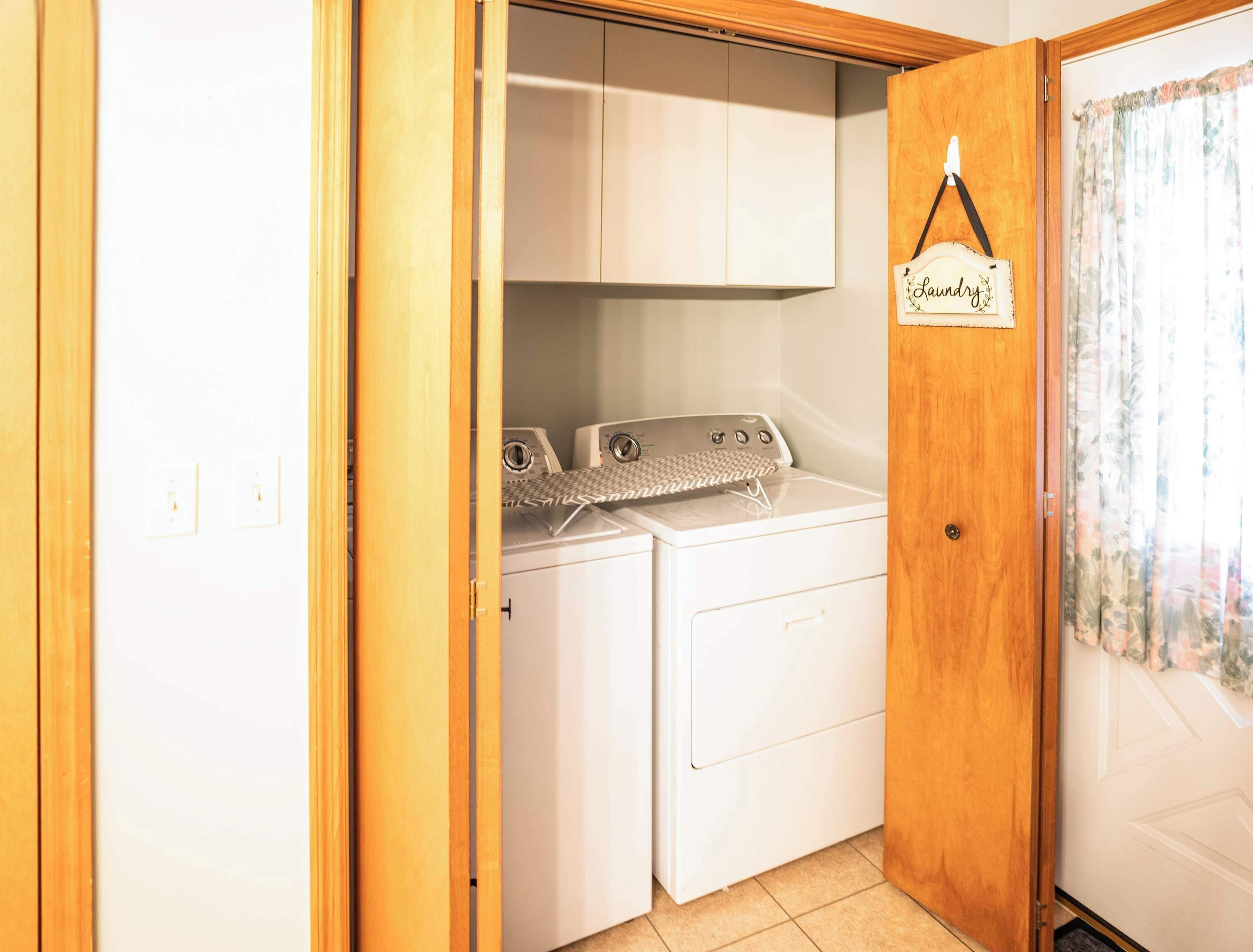 Un cuarto de lavandería con dos lavadoras y una secadora, puerta de madera y un letrero que dice 'Laundry'.