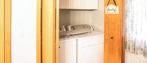 Un cuarto de lavandería con dos lavadoras y una secadora, puerta de madera y un letrero que dice 'Laundry'.