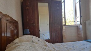 A bedroom with a wooden wardrobe, a bed with a patterned duvet, a bedside lamp, and a window with a view of trees. - Rebellat - SAINT-JULIEN-DU-PUY (SAINT-JULIEN-DU-PUY)
