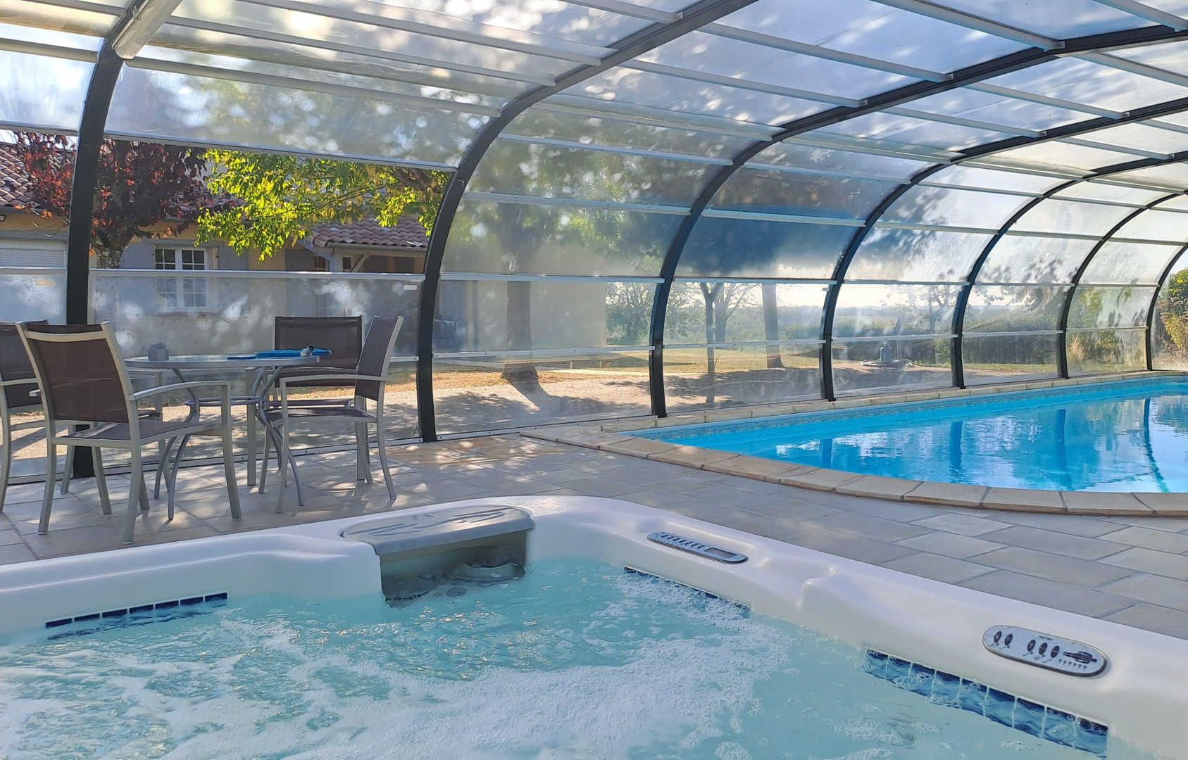 A covered swimming pool with a hot tub, surrounded by patio furniture and a glass enclosure.