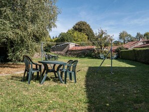 Eine Terrasse mit Tisch und Stühlen, umgeben von einer Hecke und Bäumen.