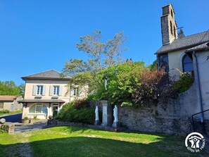 Ein traditionelles Steinhaus mit einer Statue davor, einem gepflegten Rasen und blauem Himmel.
