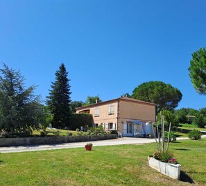 Une maison à deux étages, avec un toit recouvert de tuiles, entourée d’une pelouse bien entretenue et d’arbres.