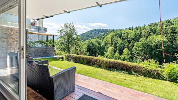 A patio with wicker furniture, a glass door, and a view of a forested hillside. - Apartment 'Burkhardt' with Mountain View, Private Terrace and Wi-Fi (Bad Herrenalb)