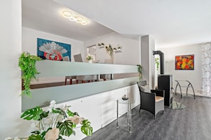 Een modern interieur met een glazen scheidingswand, een bank, een fauteuil, een tafel, een open haard en wandplanters.