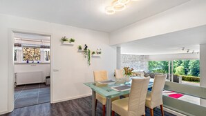A modern dining area with a glass table, white chairs, and a view of greenery outside. - Apartment 'Burkhardt' with Mountain View, Private Terrace and Wi-Fi (Bad Herrenalb)