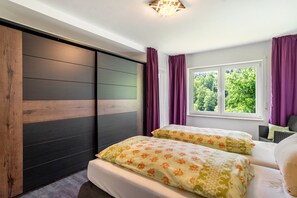 A bedroom with two beds, a window with curtains, a view of greenery, and a ceiling light fixture. - Apartment 'Burkhardt' with Mountain View, Private Terrace and Wi-Fi (Bad Herrenalb)