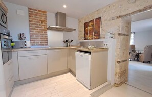 Une cuisine moderne avec un mur d’accent en briques, un lave-vaisselle et un coin repas visible à travers une porte ouverte.