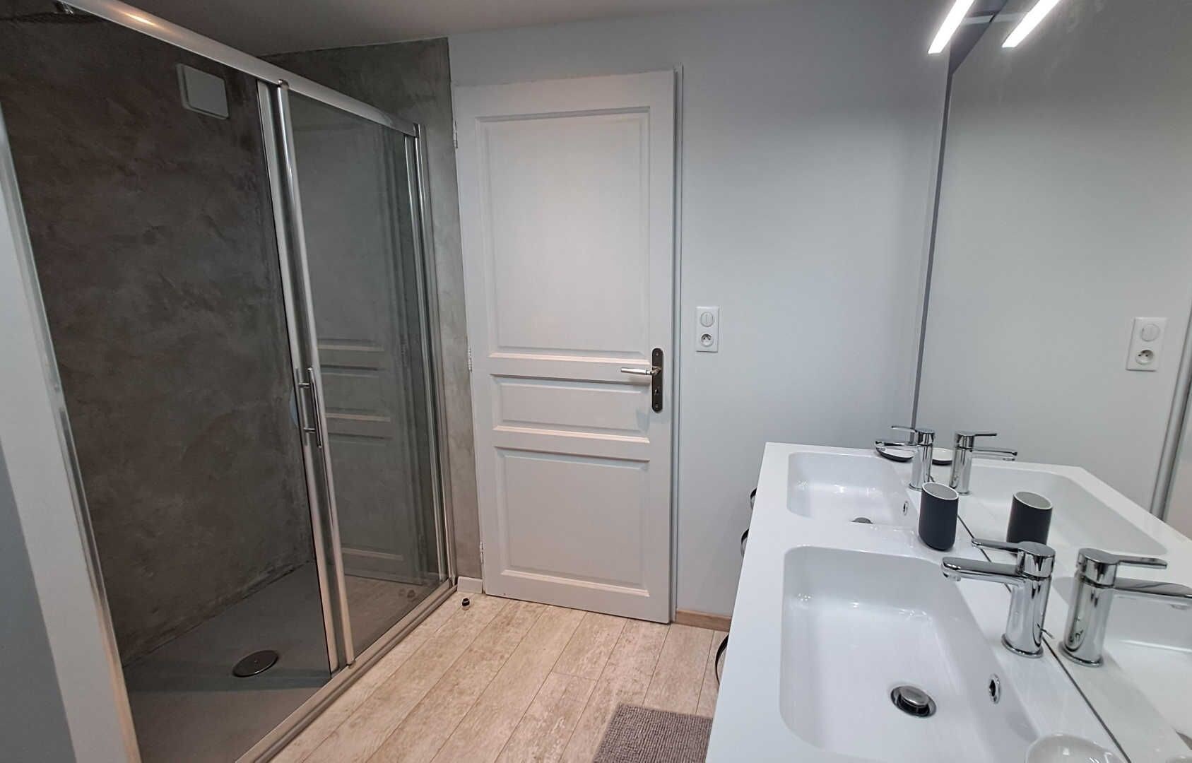 A modern bathroom with a glass shower enclosure, a white door, and a large mirror reflecting the room.