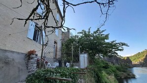 Un edificio junto al río con un muro de piedra, una cerca de metal y vistas de un río y colinas.