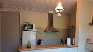 Una cocina compacta con encimera de madera, dos taburetes grises, un refrigerador blanco, un microondas y una lámpara colgante.
