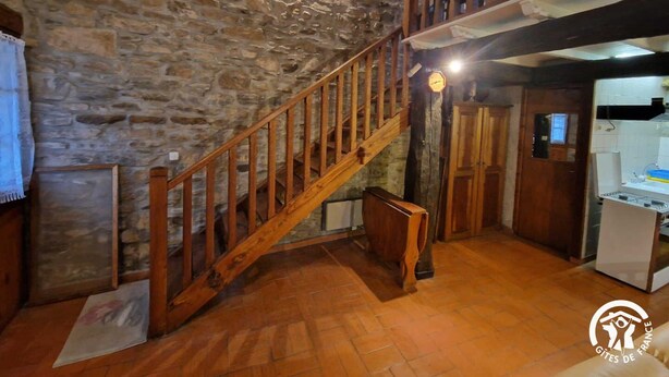A rustic interior with a stone wall, wooden staircase, and a kitchen area. - Gîte 42 - LACAUNE - Gîte (LACAUNE)